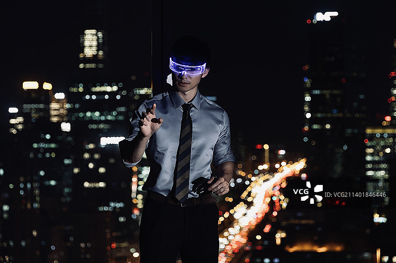 商务男人站在酒店房间戴着VR眼镜触摸虚拟智能屏幕工作图片素材