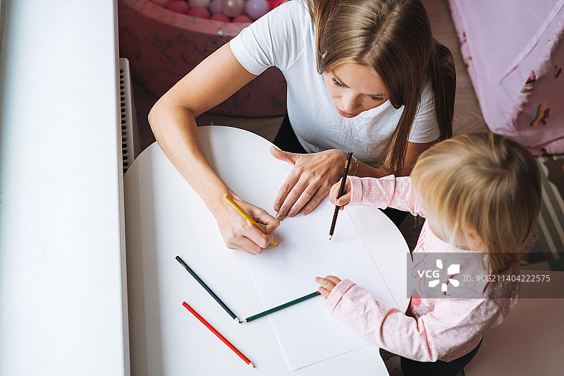 俄罗斯斯维尔德洛夫斯克州叶卡捷琳堡，一个小女孩和妈妈在儿童房的桌子上用彩色铅笔画画图片素材