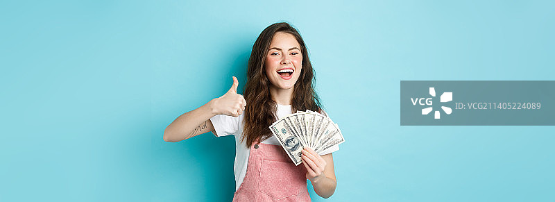 微笑快乐的女人拿着钱，美钞，竖起大拇指图片素材