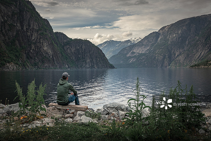 男子坐在湖边的山景观Eidfjord峡湾挪威，Eidfjord，挪威图片素材