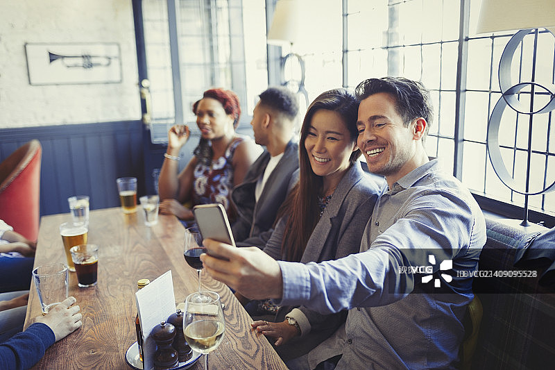 一对微笑的情侣在酒吧的餐桌上用手机自拍图片素材