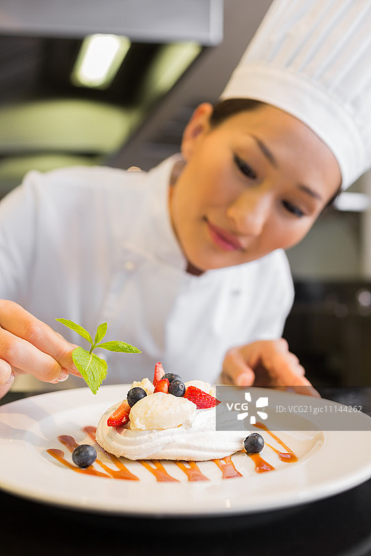 一个专注的女厨师在厨房装饰食物的特写图片素材