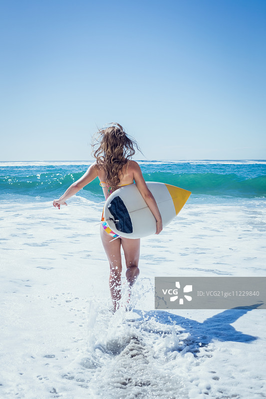 在一个阳光明媚的日子里，健康的冲浪女孩带着她的冲浪板跑到海边图片素材