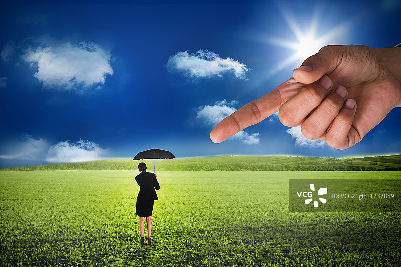 巨大的手指向年轻的女商人撑着伞，对着阳光明媚的绿色景观图片素材