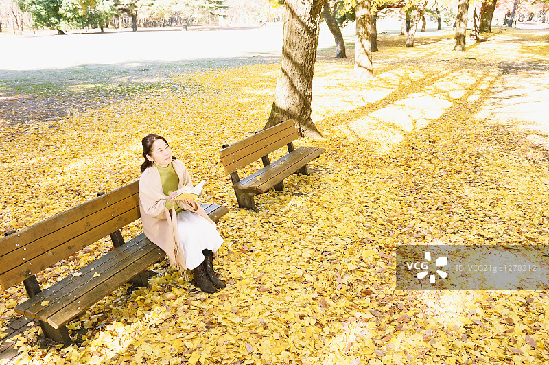一位日本老妇人坐在长椅上，手里拿着一本书图片素材