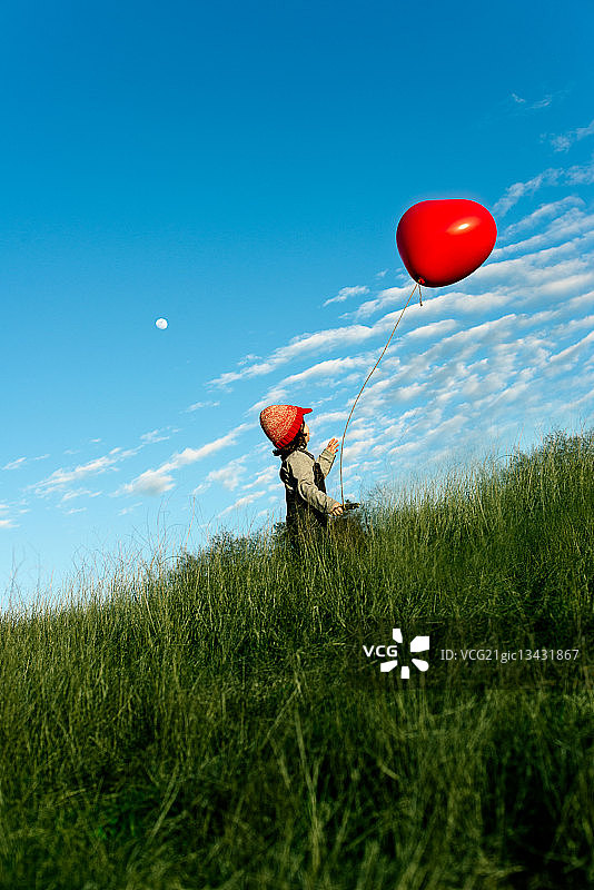 男孩(6-7)与红色气球在草地上图片素材
