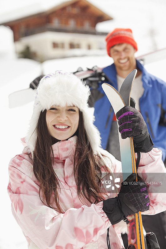 带着滑雪板微笑的夫妇在小屋外的肖像图片素材