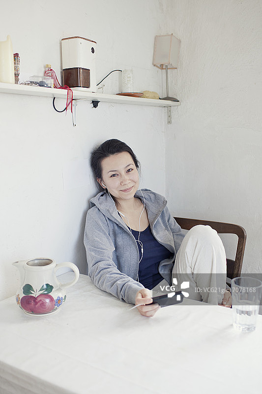 一个年轻女人坐在厨房里听mp3图片素材