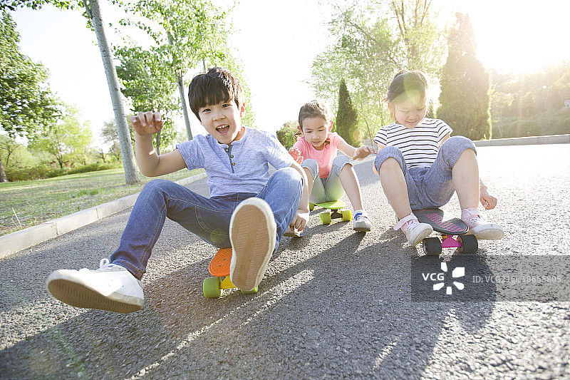 快乐的儿童坐在滑板上往前滑图片素材
