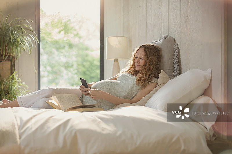 孕妇躺在床上看书，用手机发短信图片素材