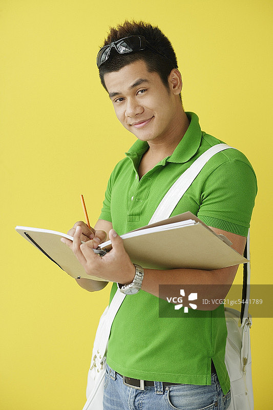 一个人站在黄色的背景下，在笔记本上写着什么，看着相机图片素材