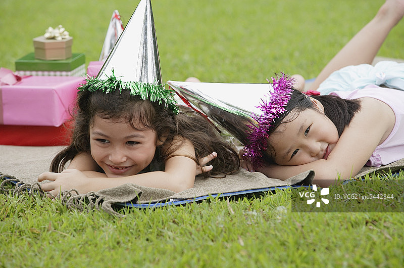两个女孩戴着派对帽躺在野餐毯子上休息图片素材