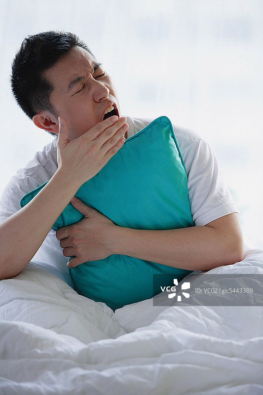 男人坐在床上，抱着枕头，打哈欠图片素材