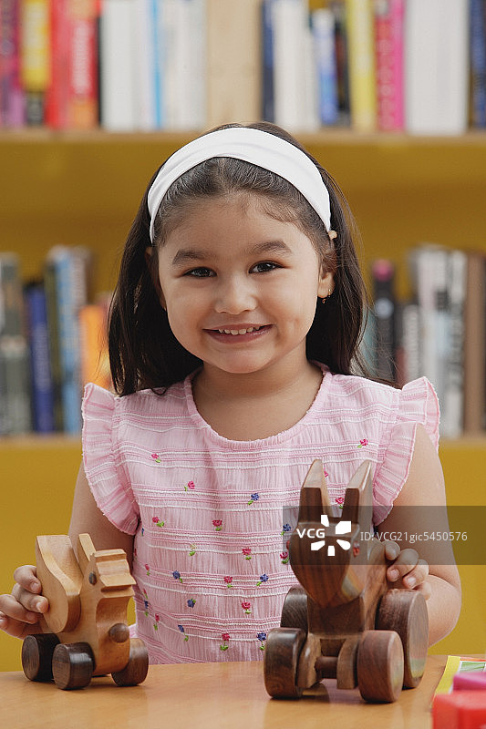 小女孩拿着木制玩具，对着镜头微笑图片素材
