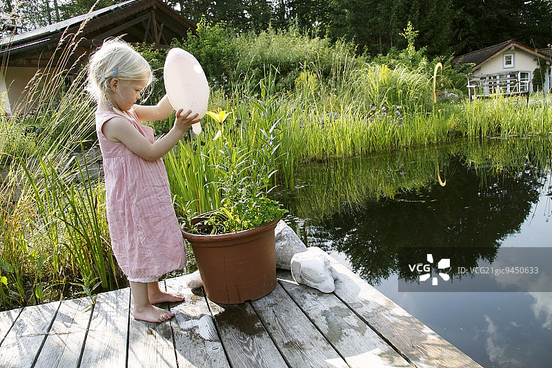 金发女孩在花园池塘边给盆栽浇水图片素材