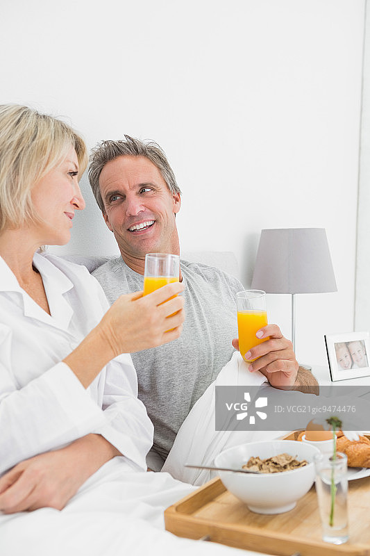 微笑的夫妇在卧室的床上喝着橙汁吃早餐图片素材