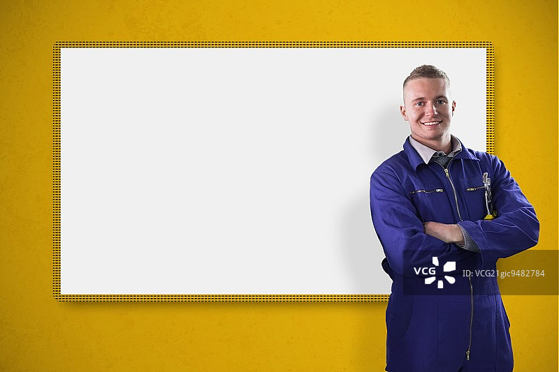 微笑的机械师站在黄色背景的白色屏幕前图片素材