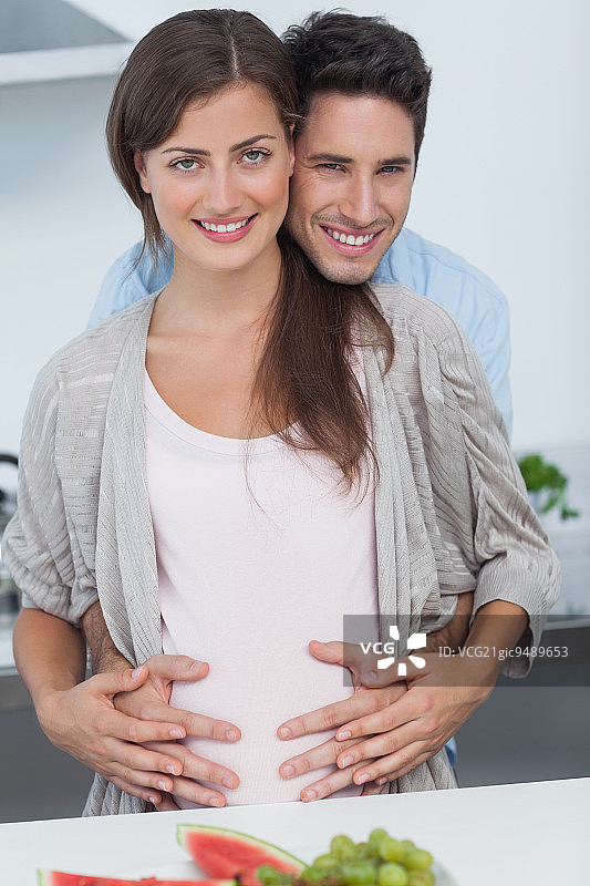 一个男人在厨房里抱着他怀孕的妻子的肚子图片素材