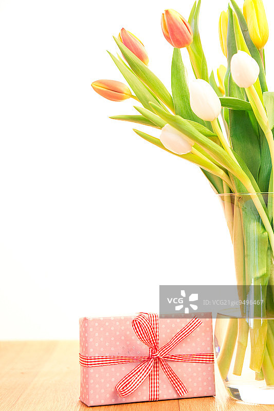 木桌上放着一瓶郁金香，还有粉红色包装的礼物图片素材