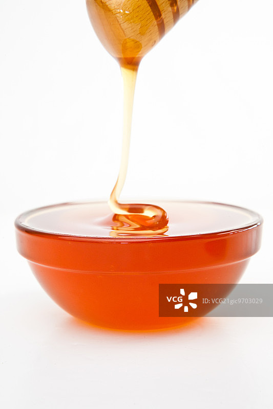 蜂蜜在白色的背景下滴落在装满蜂蜜的碗里图片素材