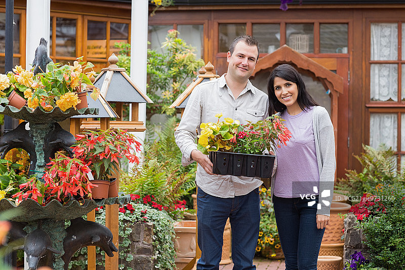 一对夫妇面带微笑，在花园中心端着一托盘植物图片素材