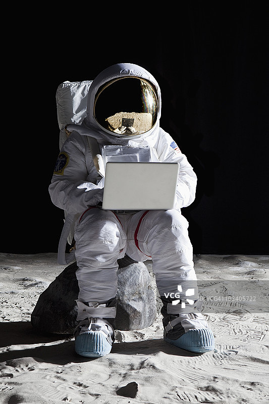 月球上的宇航员坐在一块岩石上用笔记本电脑图片素材