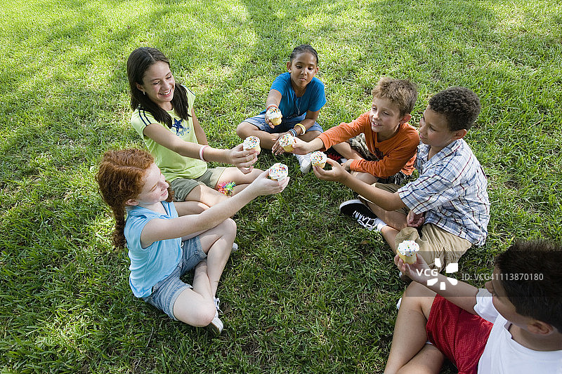 在一个公园里，孩子们围坐在一起为纸杯蛋糕欢呼图片素材