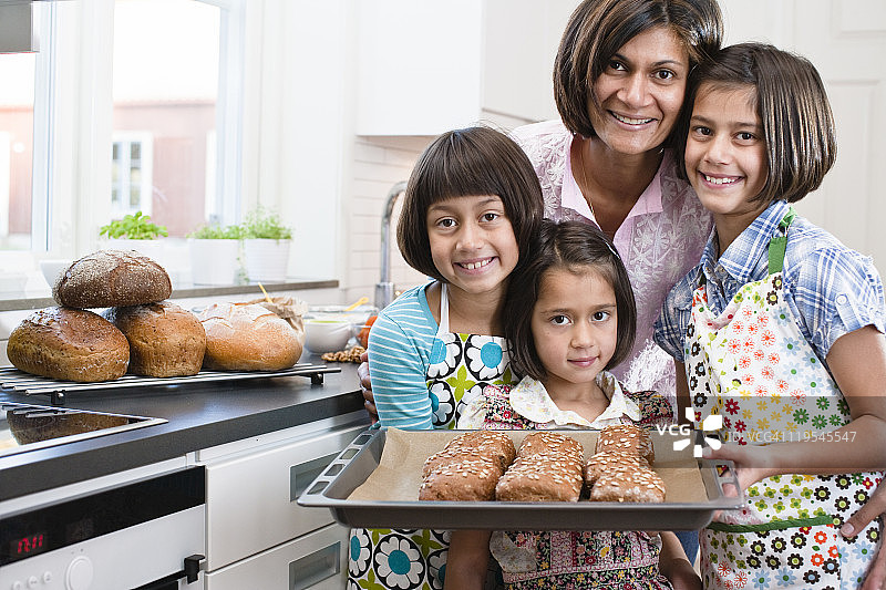 母亲和三个女儿的画像，她们都吃着刚做好的面包卷图片素材
