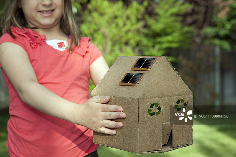 女孩拿着一个装着太阳能板的纸板房子图片素材
