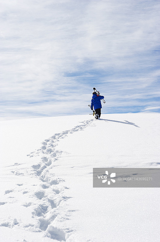 孩子背着滑雪板登上雪山图片素材