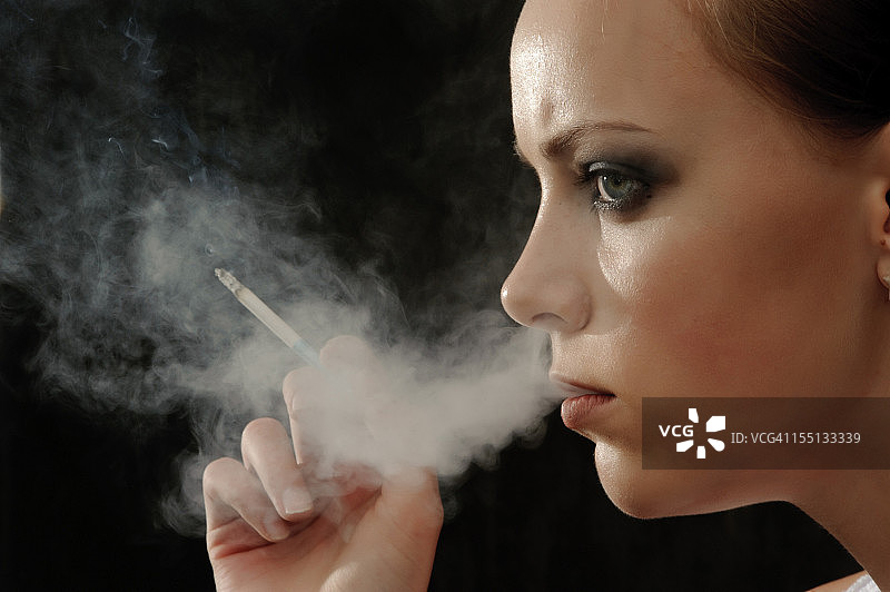 年轻女子侧面抽烟，从鼻子里吐出烟来图片素材