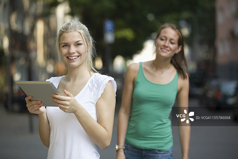 德国，北莱茵威斯特伐利亚，科隆，年轻女性在街上拿着平板电脑微笑着图片素材