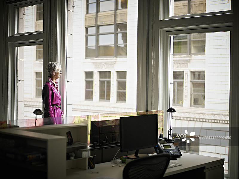 从办公室窗户往外看的资深女商人图片素材