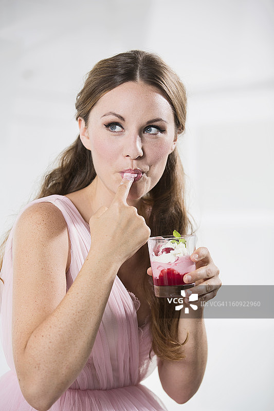 德国，年轻女子端着一杯酸奶，舔着手指图片素材