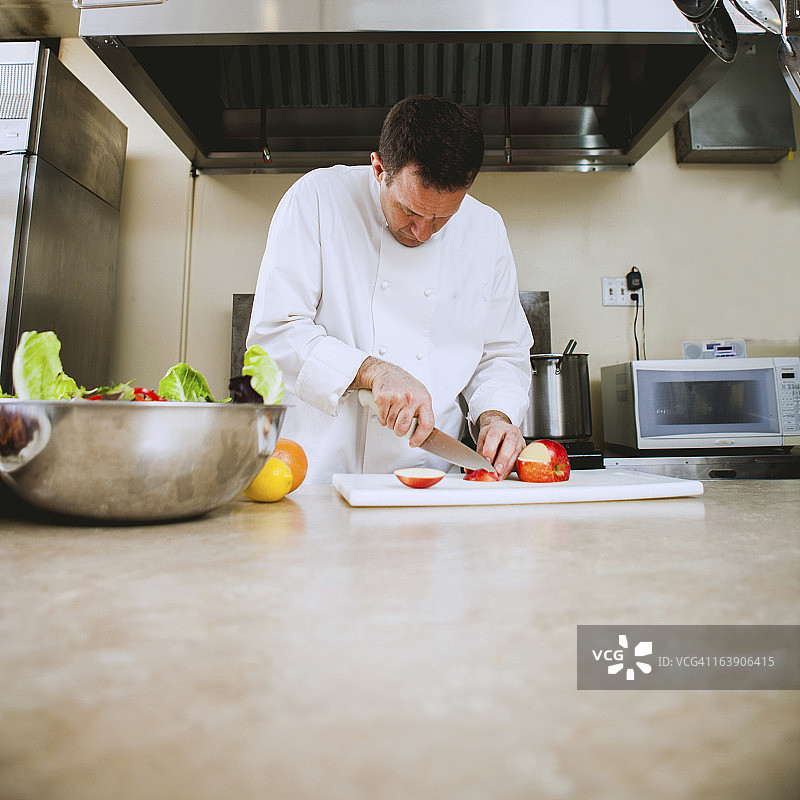 白种男厨师在繁忙的餐厅厨房里切水果图片素材