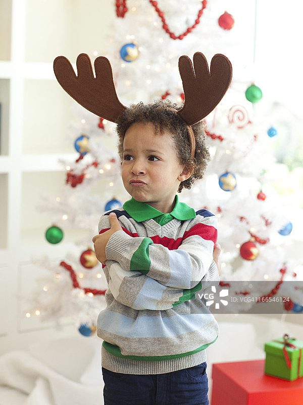 快乐的小男孩鹿角站在圣诞树前图片素材