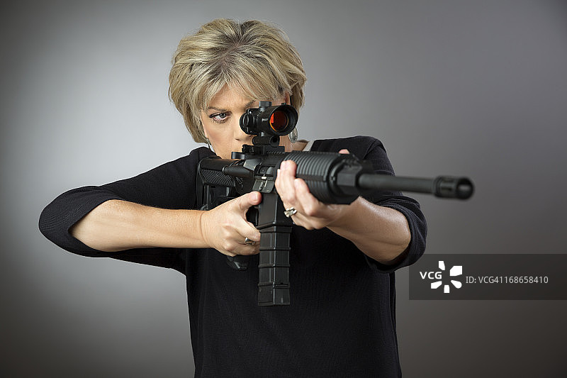 一个成熟的女人在灰色的背景下盯着步枪图片素材