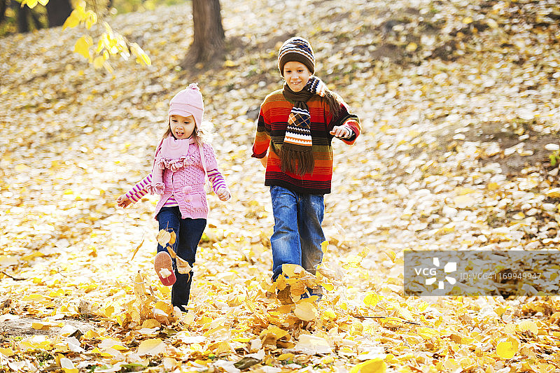 两个可爱的孩子在满是树叶的公园里奔跑。图片素材