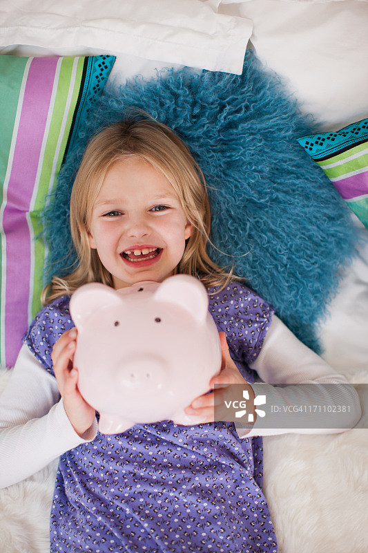 咧嘴笑的女孩躺在床上的小猪存钱罐图片素材