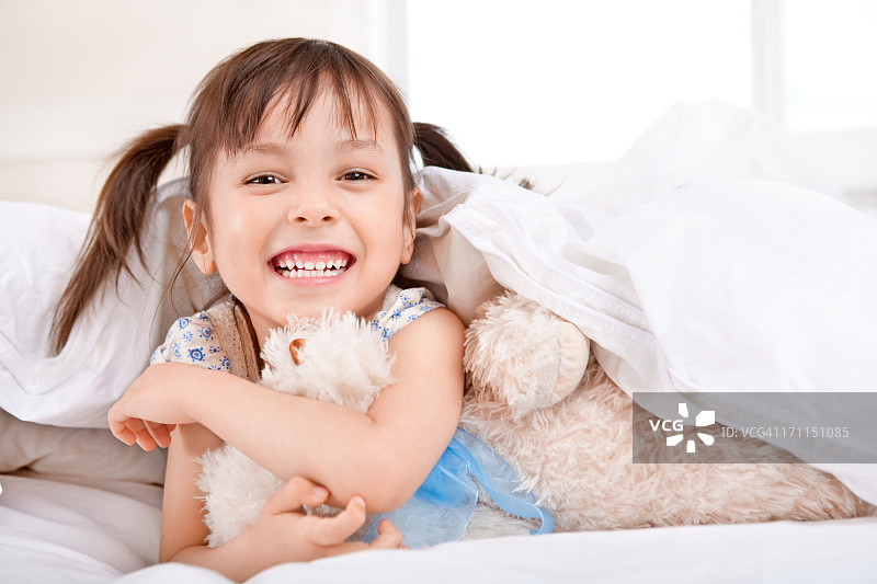 快乐的小女孩躺在毯子下和泰迪熊图片素材