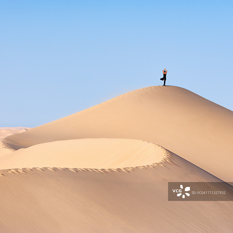 一名年轻女子在撒哈拉沙漠上练习瑜伽图片素材