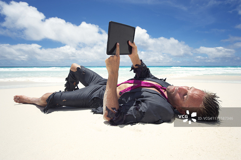漂流商人放松与数字平板电脑在海滩上图片素材