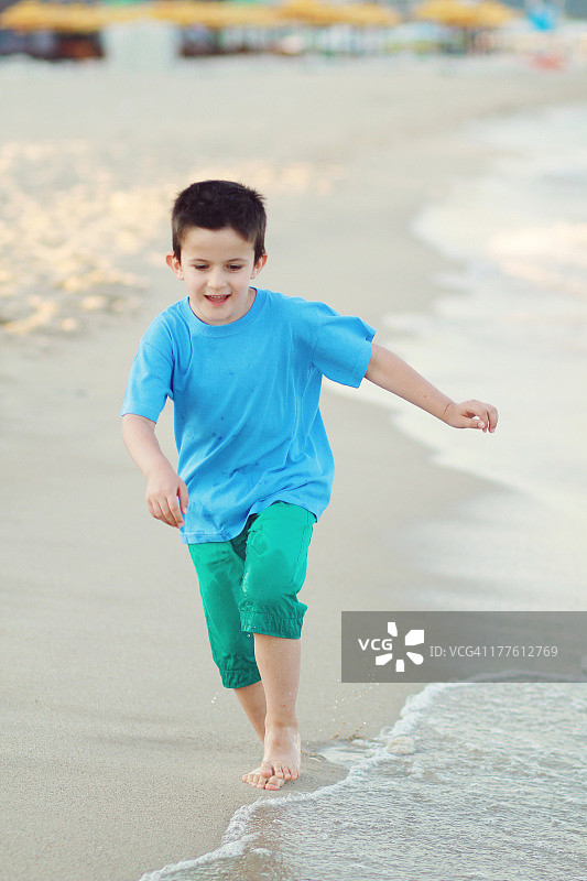 可爱的男孩赤脚在沙滩上跑步和玩耍图片素材