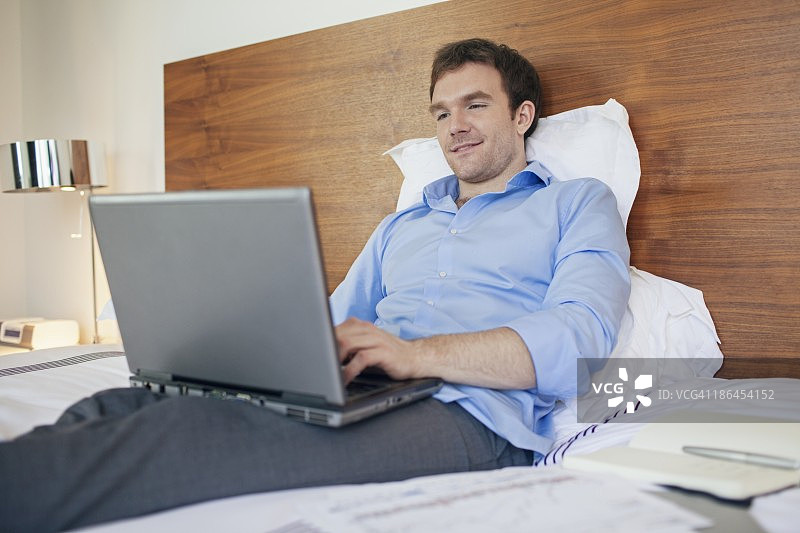 商人躺在床上用笔记本电脑图片素材