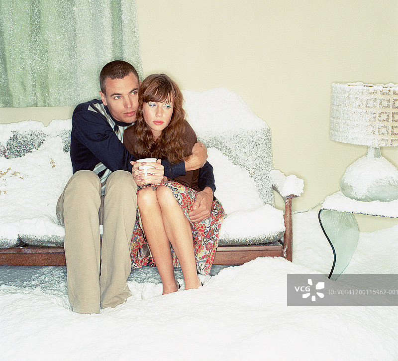 在白雪覆盖的房间里，一对情侣在沙发上拥抱图片素材