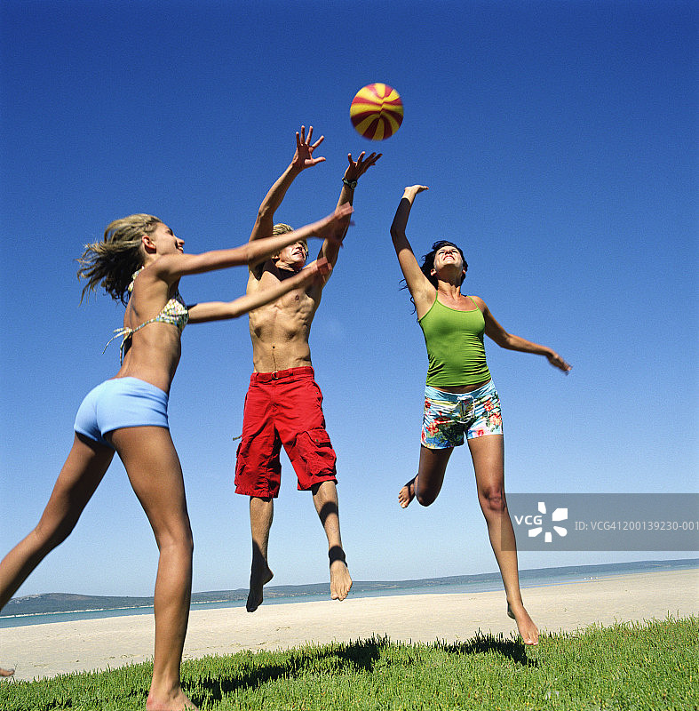 三个年轻人在海滩上跳着去接球图片素材