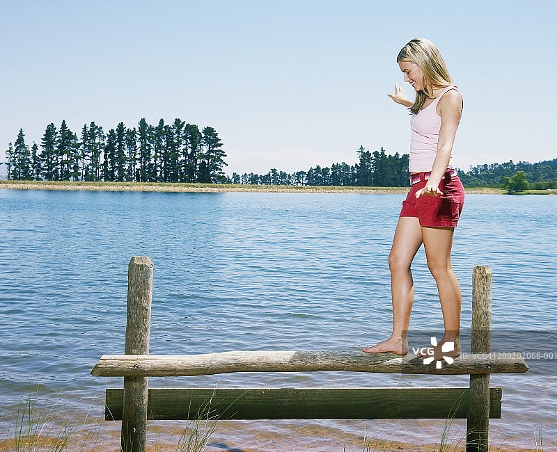 十几岁的女孩(13-15岁)在湖边的木栅栏上保持平衡图片素材