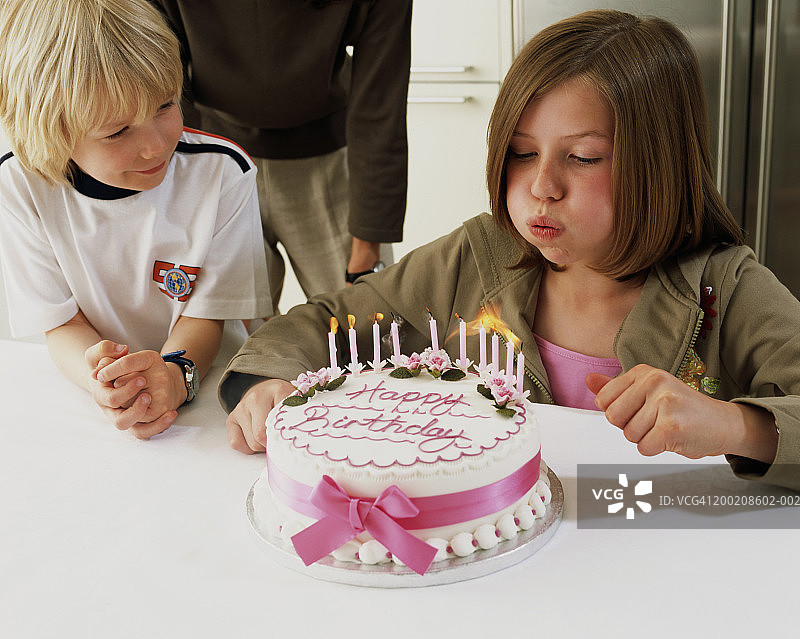 男孩(5-7)看着姐姐(10-12)吹灭生日蛋糕上的蜡烛图片素材