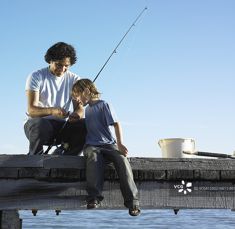父亲微笑着教儿子(4-6)如何在码头上钓鱼图片素材
