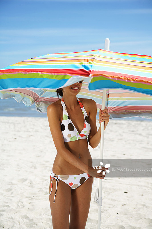 年轻女子站在沙滩伞下，微笑，特写图片素材